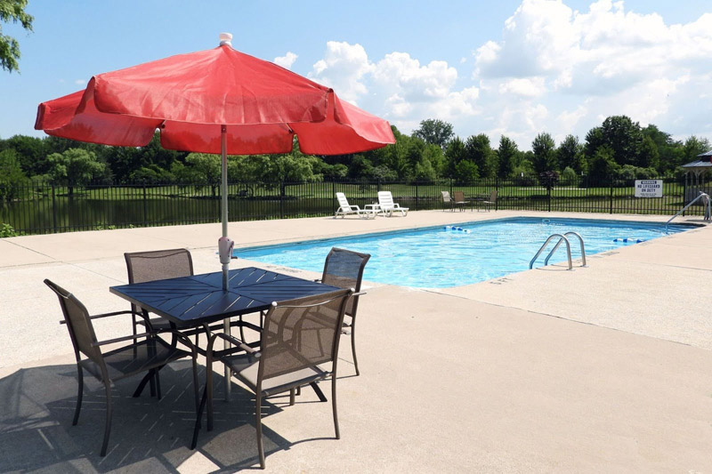 Outdoor swimming pool with patio seating and lake view at Spring Lake manufactured home community in Stevensville, Michigan