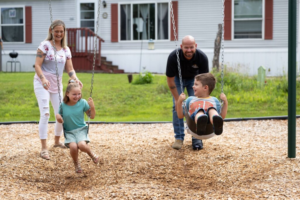 Family enjoying playground swings in a manufactured home community. 